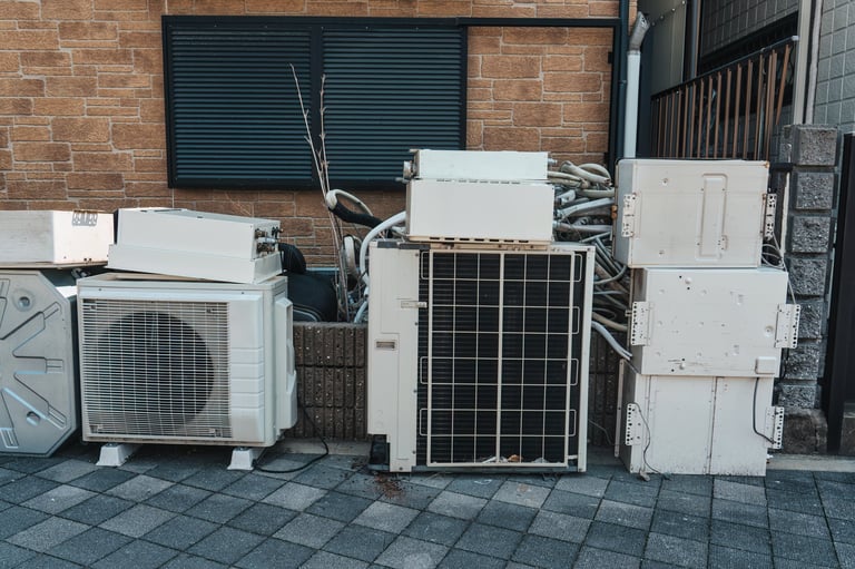 Damaged and used old air conditioner units, compressor, electrical components stacked beside residential building wall in urban