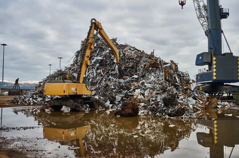 Yellow excavator sorting through scrap metal at industrial junkyard