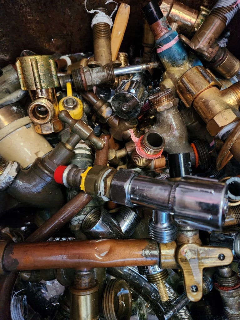 Collection of used brass plumbing fixtures and metal valves piled together including copper pipes and ball valves